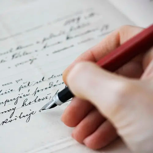 Un primer plano de una mano escribiendo elegantemente con una pluma estilográfica de cuerpo rojo sobre un papel antiguo con caligrafía manuscrita.